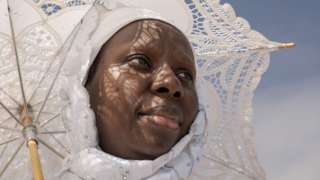 A woman dressed in white carries a matching white, lace parasol.