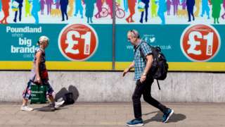 People carrying shopping bags make their way past a window advertisement for Poundland