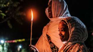 A woman and girl holding at candle at the Fasilides Bath during Timket in Gondar, Ethiopia - Wednesday 19 January 2022
