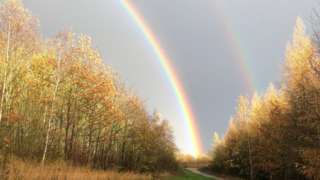 A person walking along a path under a double rainbow