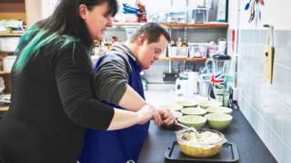 Caregiver teaching Down's syndrome student in a kitchen (stock photo)