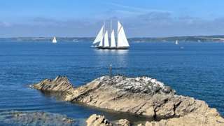 Rocks by a coastline with a sailing boat in the distance