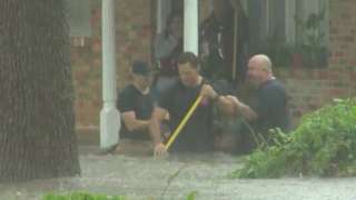 Three rescuers, waist-deep in flood water, help residents from their home.