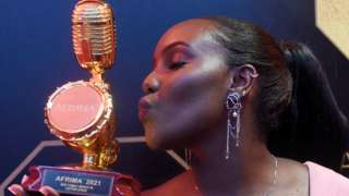 Nikita Kering wearing a pink outfit posing for a picture, kissing an award. She is holding another award in her other hand - Lagos, Nigeria Sunday 21 November 2021