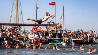 Man in swim shorts reaches for red flag during slippery pole event at Mersea Regatta