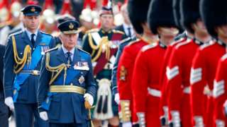King Charles and Prince William in a procession, in military uniforms, alongside Guards in bearskins
