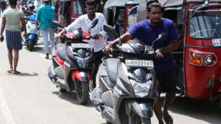 Two motorbike riders push bikes as fuel sales are banned in Sri Lanka