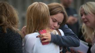 A young girl hugs her friend tightly after they receive their a-level results