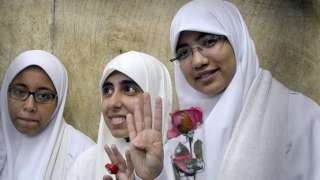Egyptian women members of the Muslim Brotherhood hold roses and show a four-finger sign, called Rabaa (four) in Arabic, the as they stand in the defendants' cage during their trial in at the court in the Egyptian Mediterranean city of Alexandria on December 7, 2013
