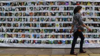 A person walks past a banner displaying the photos of the 242 people who died in the 2013 fire at the Kiss nightclub, during a trial against the accused, in Porto Alegre, Brazil, on December 1, 2021.