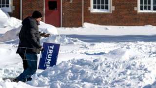 A man carries in Trump sign in the snow in Iowa