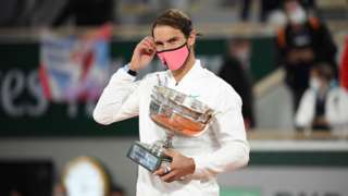 Rafael Nadal adjusts his facemask while holding the French Open trophy