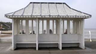 People sitting in a weather shelter on Cromer Pier, Norfolk