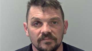 Mugshot of David Perry. He is white with dark hair and a bloodshot right eye, He also has a dark moustache and short beard.