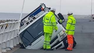 Bin lorry in a hole on Rhyl promenade, with two workmen nearby