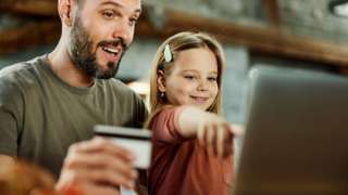 Father using credit card while shopping online with his daughter over a computer at home.
