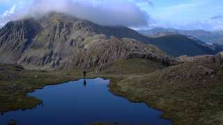 A person reflected in water by a mountain