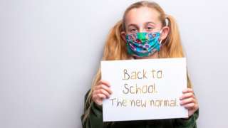 Girl wearing a mask and holding up a sign
