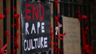 A placard saying 'End Rape Culture' attached to the fence outside a London school