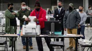 A Fulton County election worker puts absentee ballots in a scanner as election observers look on, at the Georgia World Congress Center in Atlanta, Georgia, January 5, 2021