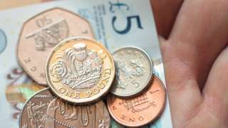 A selection of coins lie on top of a five pound note held in someone's hand
