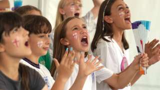Children with England flags drawn on their faces cheer and clap