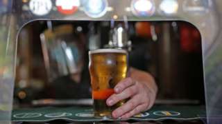 Man serves pint from behind plastic screen