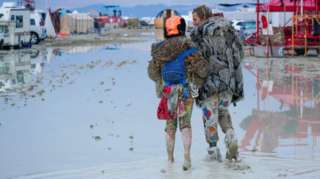 Dub Kitty and Ben Joos, of Idaho and Nevada, walk through the mud at Burning Man after a night of dancing with friends in Black Rock City, in the Nevada desert