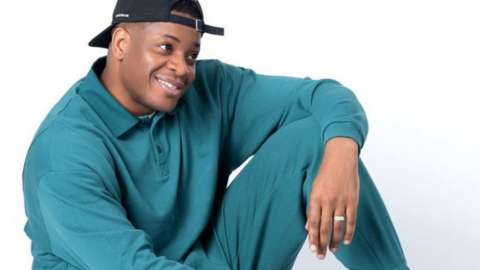 Tolu Ogunmefun sitting on the floor with his knee up, posing in a turquoise tracksuit and cap