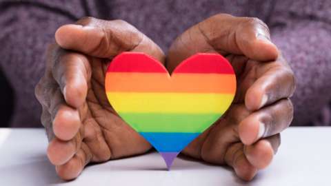 A person with their hands around a rainbow heart cut-out