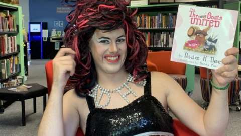 The Drag Queen, Aida H Dee, holds her book smiling after a Drag Queen Story Hour event in Cowbridge