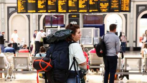 A woman with a rucksack waits in front of a departures board