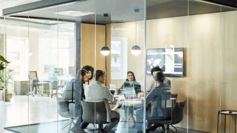 Business colleagues sitting at conference table seen through glass wall.