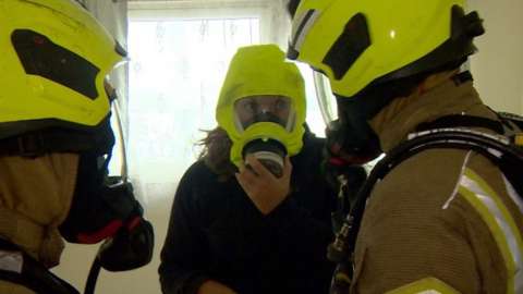 Firefighters fit a woman with a smoke hood