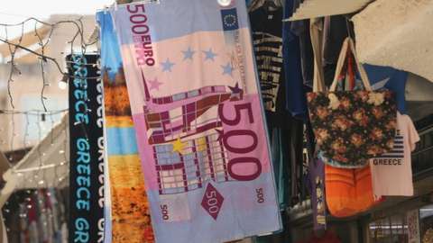 A beach towel in the image of a 500 euro note outside a souvenir shop in Greece