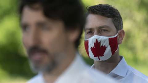 Local Member of Parliament William Amos wear a Canadian flag mask as Prime Minister Justin Trudeau speaks during a news conference in Chelsea, Quebec
