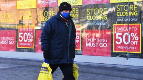 Man walking past shop with 'closing down' signs