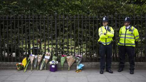 Police personnel stand beside floral tributes left in London's Russell Square on August 4, 2016, following an overnight stabbing spree that left one woman dead and five others injured.