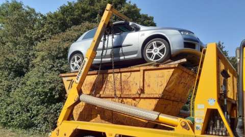 Lorry transporting a skip and a car