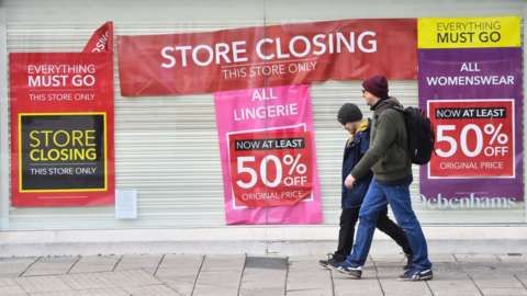 Men walking past a shut-down Debenhams store