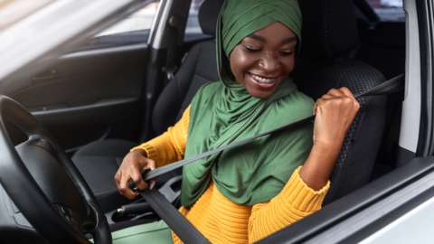A young woman puts on her seatbelt in driving seat