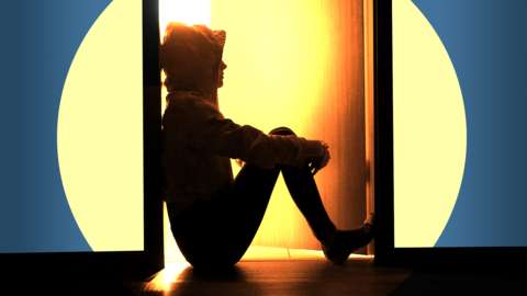 Silhouette of a teenager, in a hoodie, sitting in a doorway