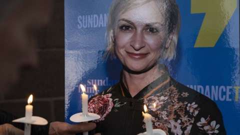 People hold candles in front of an image of Halyna Hutchins