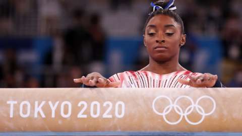 Simone Biles with her hands on a beam reading 'Tokyo 2020'