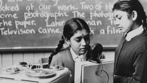 Immigrant children, learning English, 15th May 1962. Jasubin Patel, 16, and Zulekna Gora, 12 - two Indian immigrants adopted by Whetley Lane Secondary School in Bradford, Yorkshire - make a tape recording as part of a lesson to improve their English. The girls are from Bombay and are among a party of ten immigrant children drafted to the school as an experiment, after Bradford education authorities discovered that many immigrant children in the city knew so little English that they couldn't understand their lessons. '