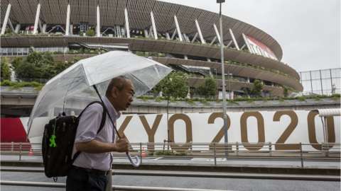 A man with an umbrella walks past the Olympic Stadium in the rain