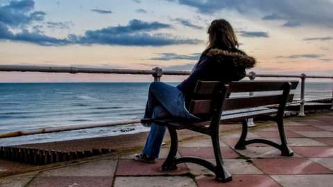Woman sat on bench next to the sea