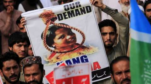 A protester holds up a poster with Asia Bibi's head in a noose above a fire pit