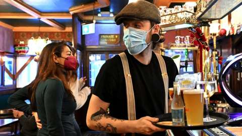 A worker wearing a face mask in Bluebell bar on High Street carries a tray of drinks to a table on December 26, 2021 in Cardiff, Wales.
