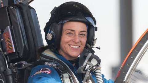 Nicole Mann sits in an aircraft smiling at camera